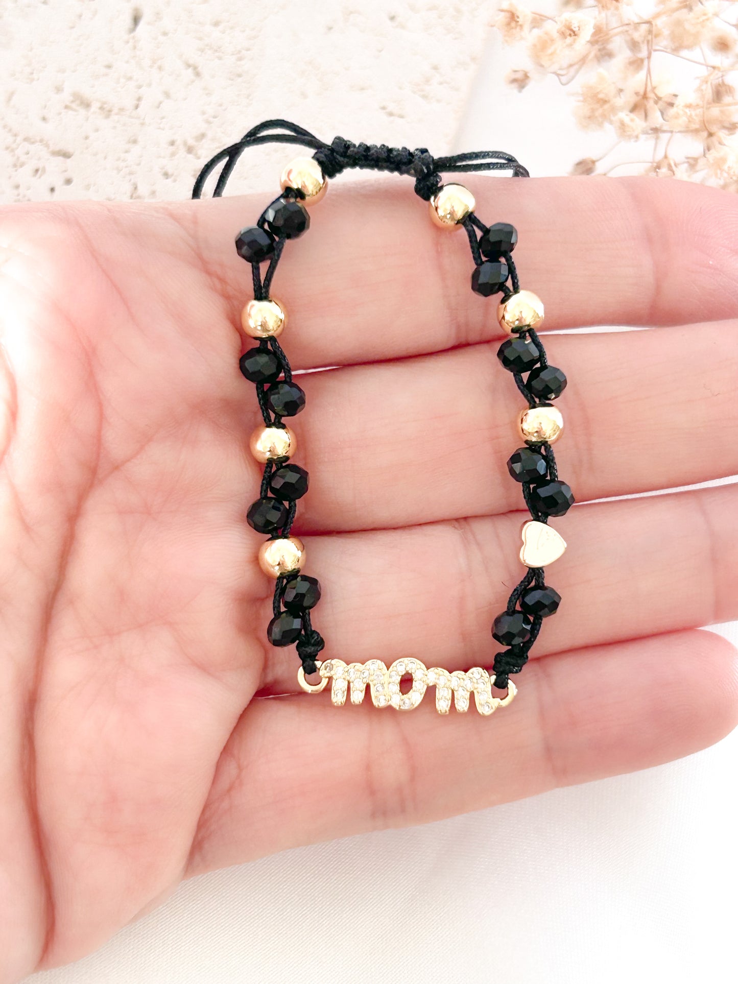 Black beaded bracelet with gold accents and 'mom' charm held in hand