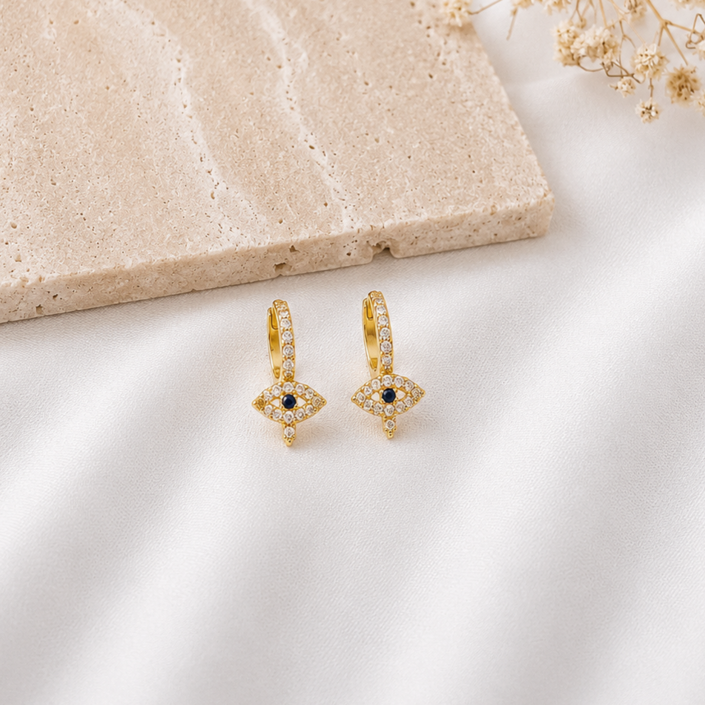 Pair of gold-tone huggie hoop earrings with sparkling cubic zirconia hoops and dangling evil eye charms featuring blue and black center stones. Elegant minimalist earrings with a protective evil eye design, perfect for everyday wear, layering, or gifting.