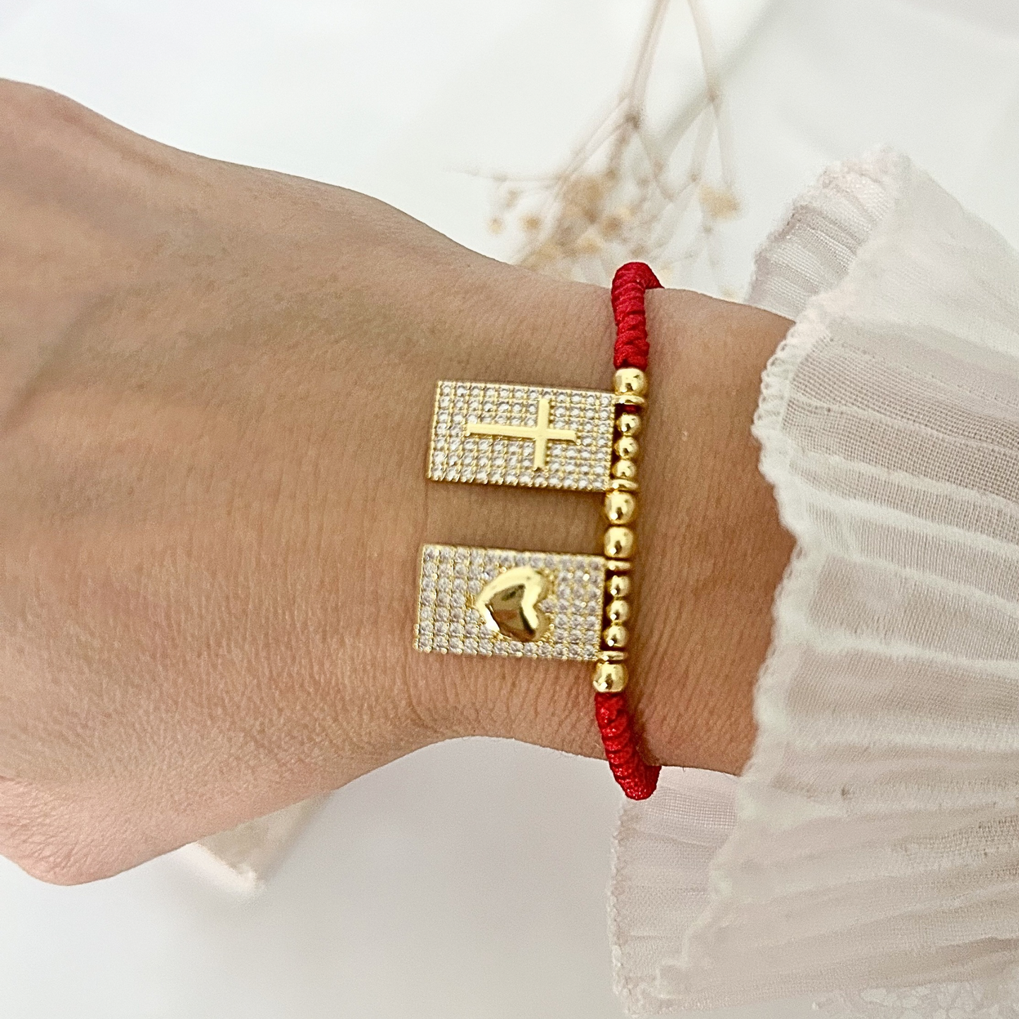 Faith-inspired bracelet worn on the wrist, showcasing red braided cord, gold-tone beads, and shimmering cross and heart charms.