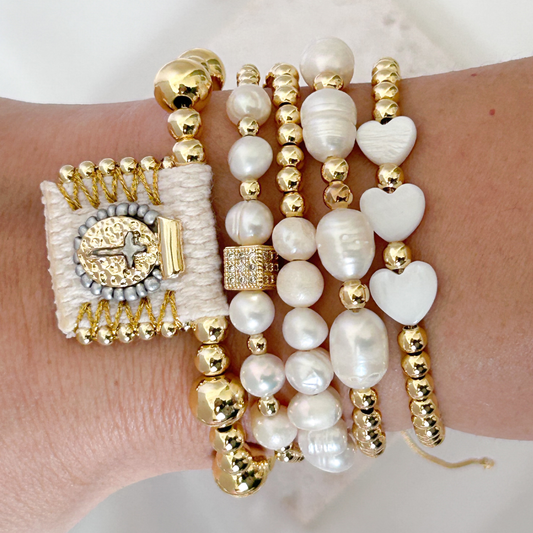 Wrist wearing multiple pearl and gold beaded bracelets on a white background