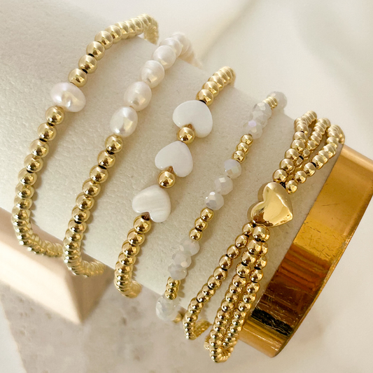 Set of gold and white beaded bracelets on a textured surface