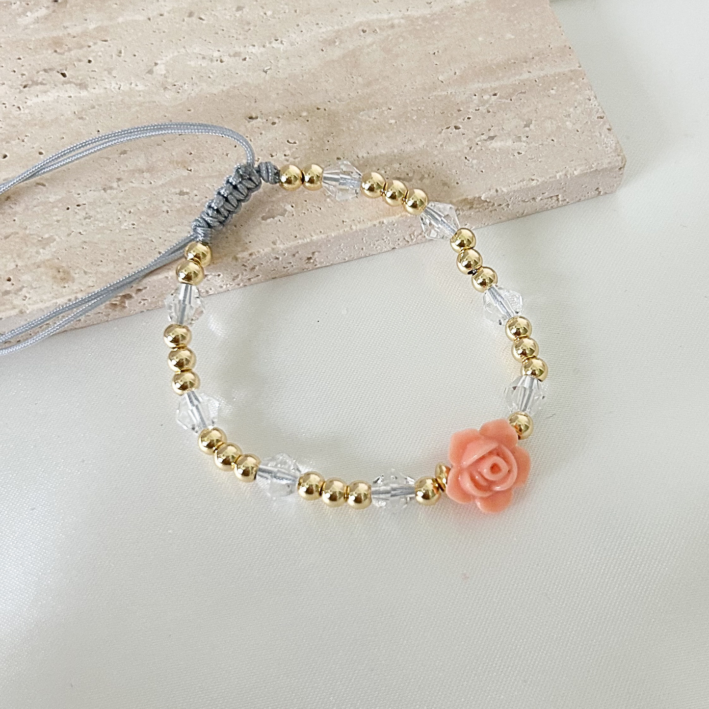 Adjustable handmade bracelet with a peach floral centerpiece, gold-tone beads, and clear crystal accents arranged on a neutral display surface.