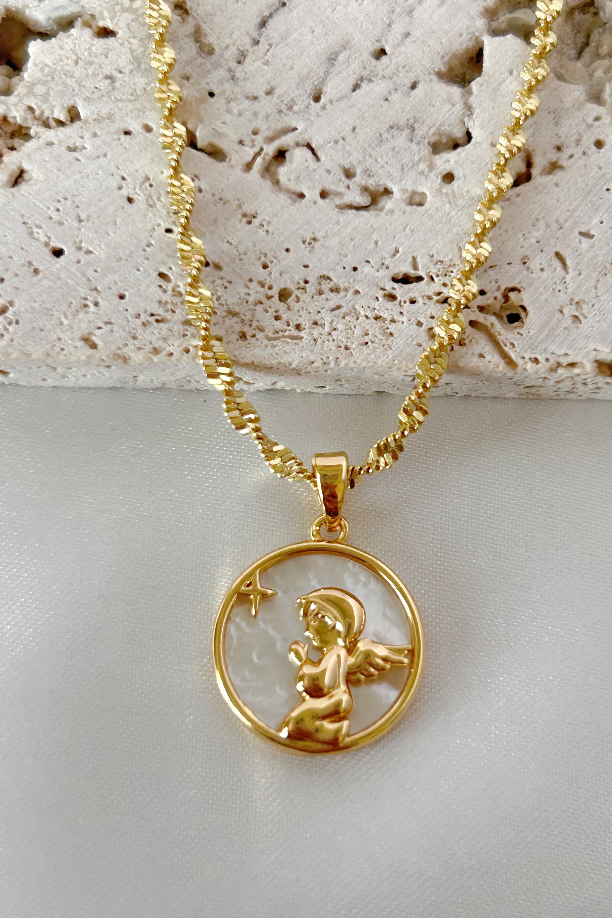 Gold necklace with an angel pendant on a textured stone surface