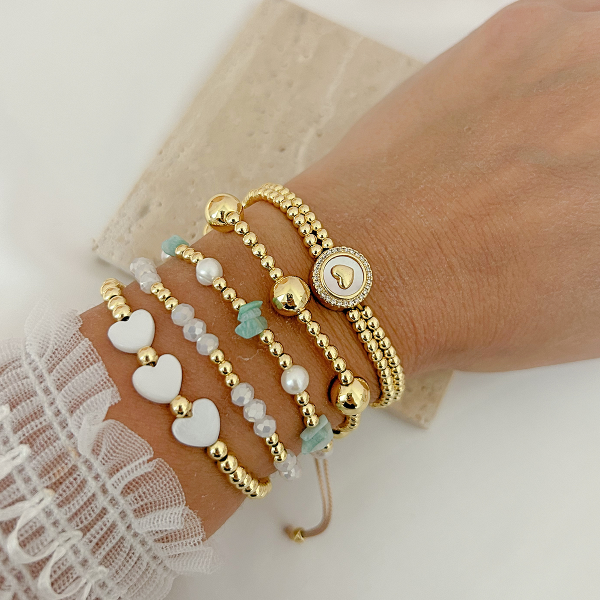 Gold bracelet stack featuring white hearts, crystal beads, turquoise accents, pearls, and a sparkling heart medallion.