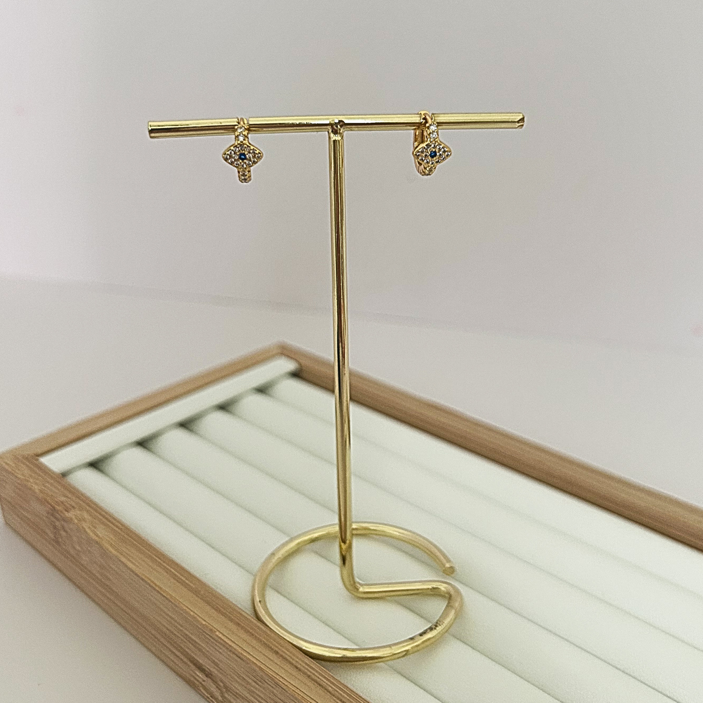 Gold huggie hoop earrings with dangling evil eye charm on jewelry stand