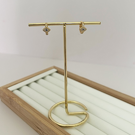 Gold huggie hoop earrings with dangling evil eye charm on jewelry stand