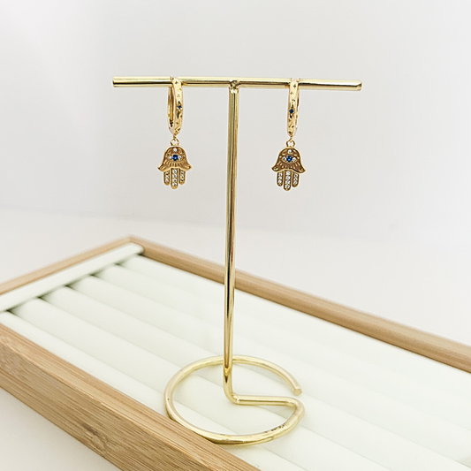 Gold hoop earrings with Hamsa hand evil eye charm on jewelry stand