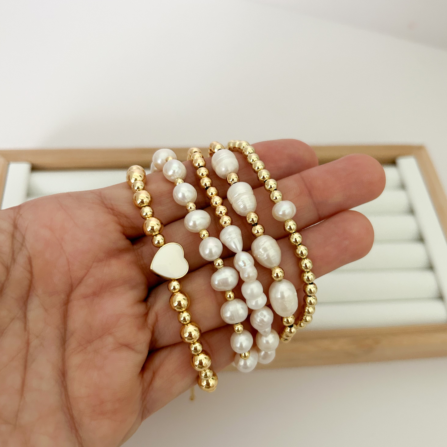 Five gold bracelets with baroque pearls and mother of pearl heart held in hand
