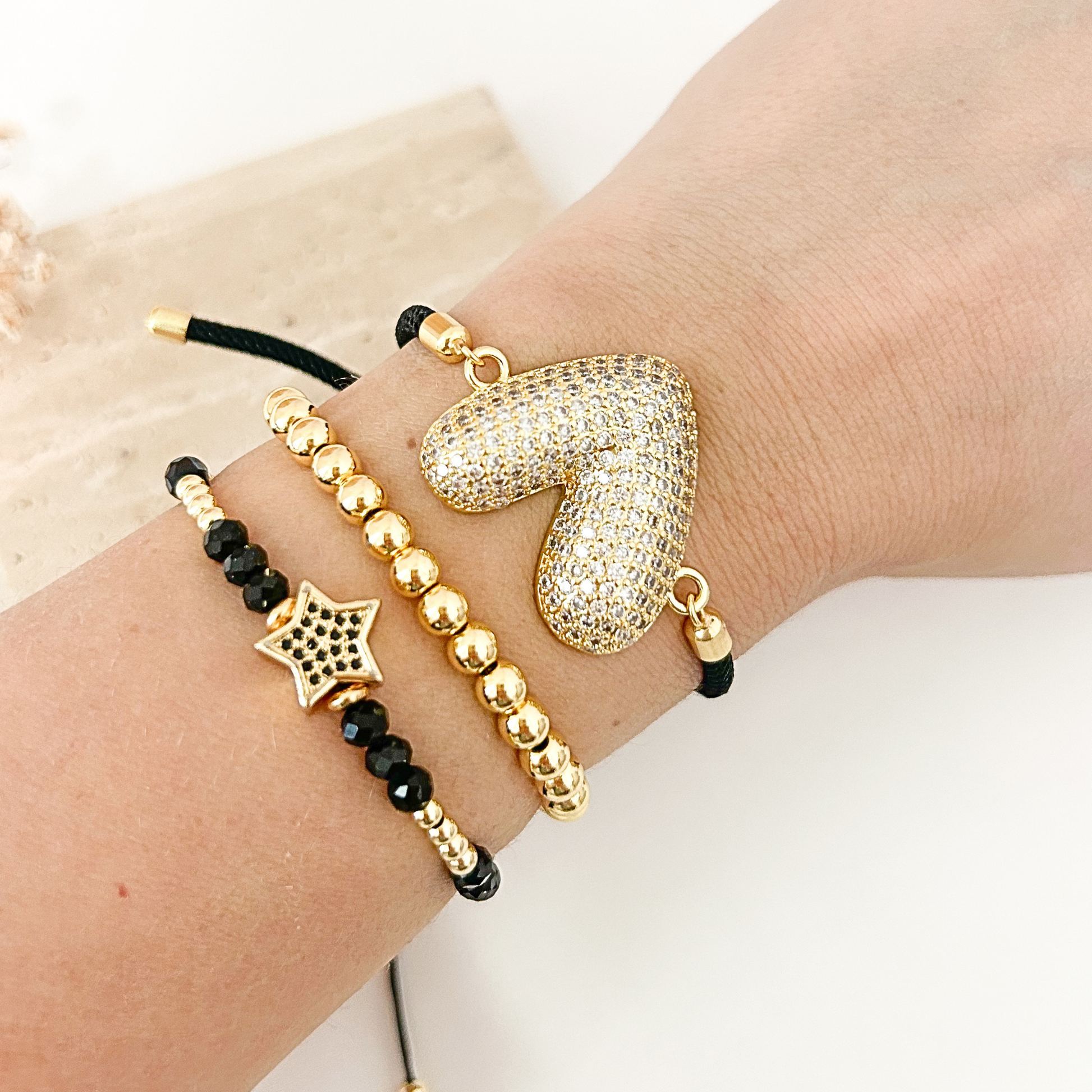 Black and gold bracelet stack featuring a pavé heart bracelet, gold beaded bracelet, and black crystal star bracelet. A stylish everyday jewelry set designed for layering or wearing individually.