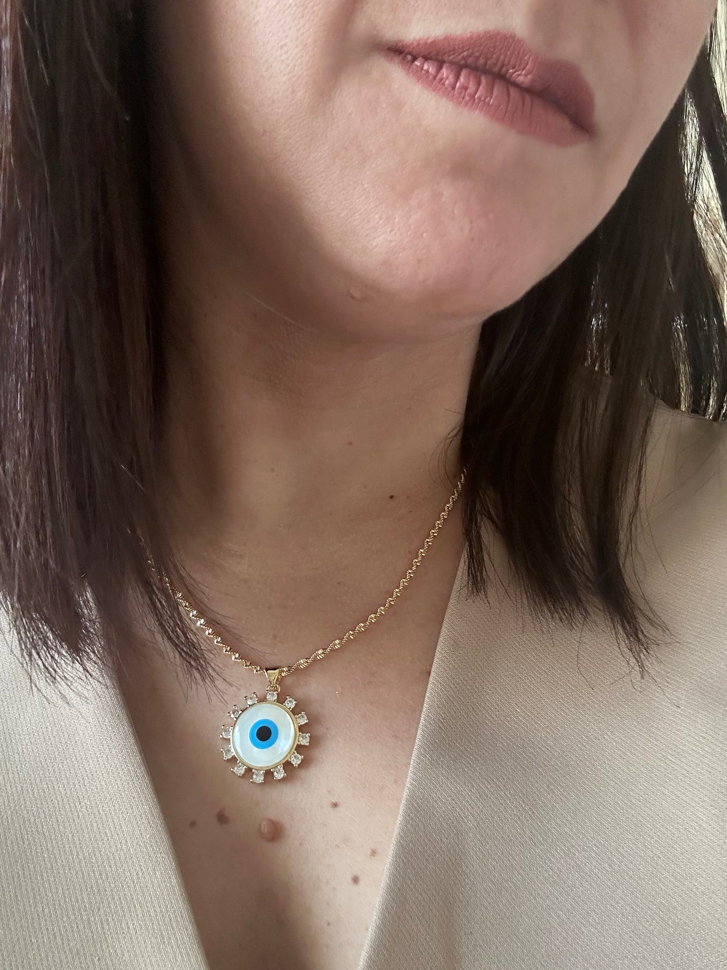 Close-up of a person wearing an eye-shaped necklace with a gold chain.