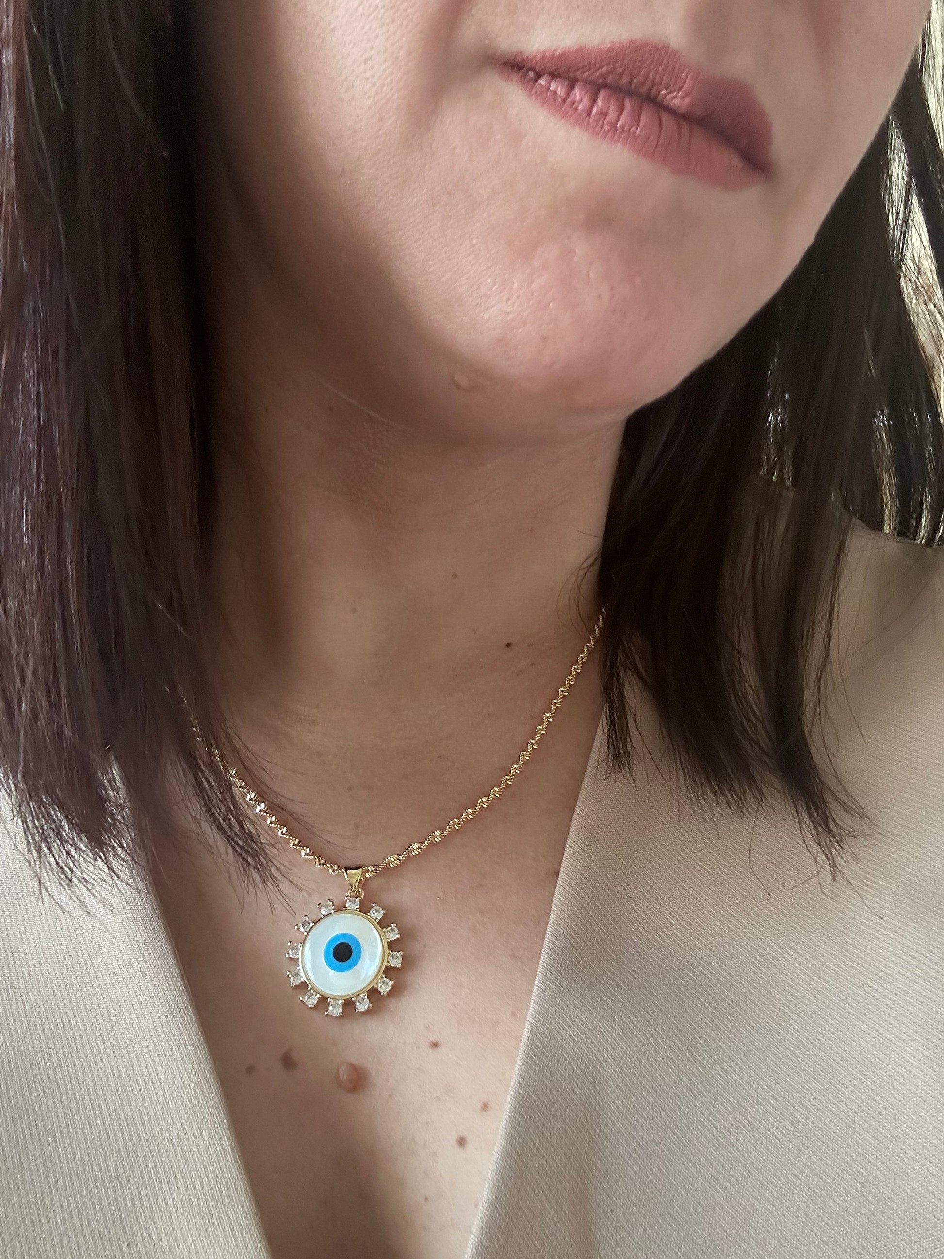 Close-up of a person wearing an eye-shaped necklace with a gold chain.
