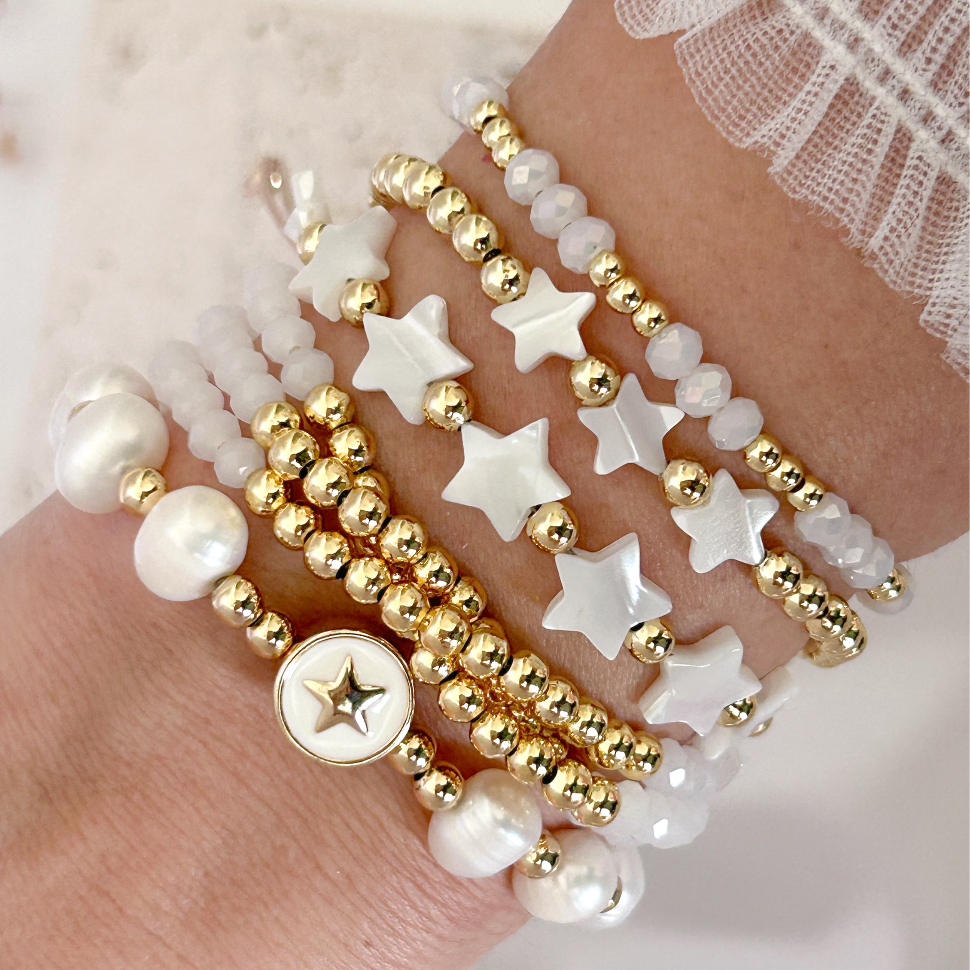 Stack of gold and white beaded bracelets on a hand against a soft background