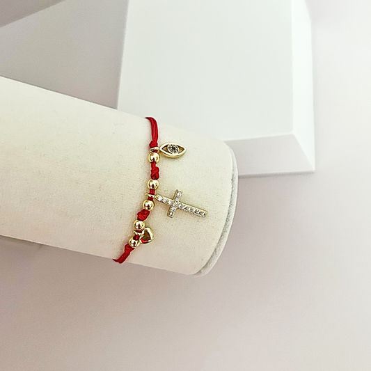 Handmade red cord bracelet with sparkling cross pendant, evil eye charm, and polished gold-tone beads.