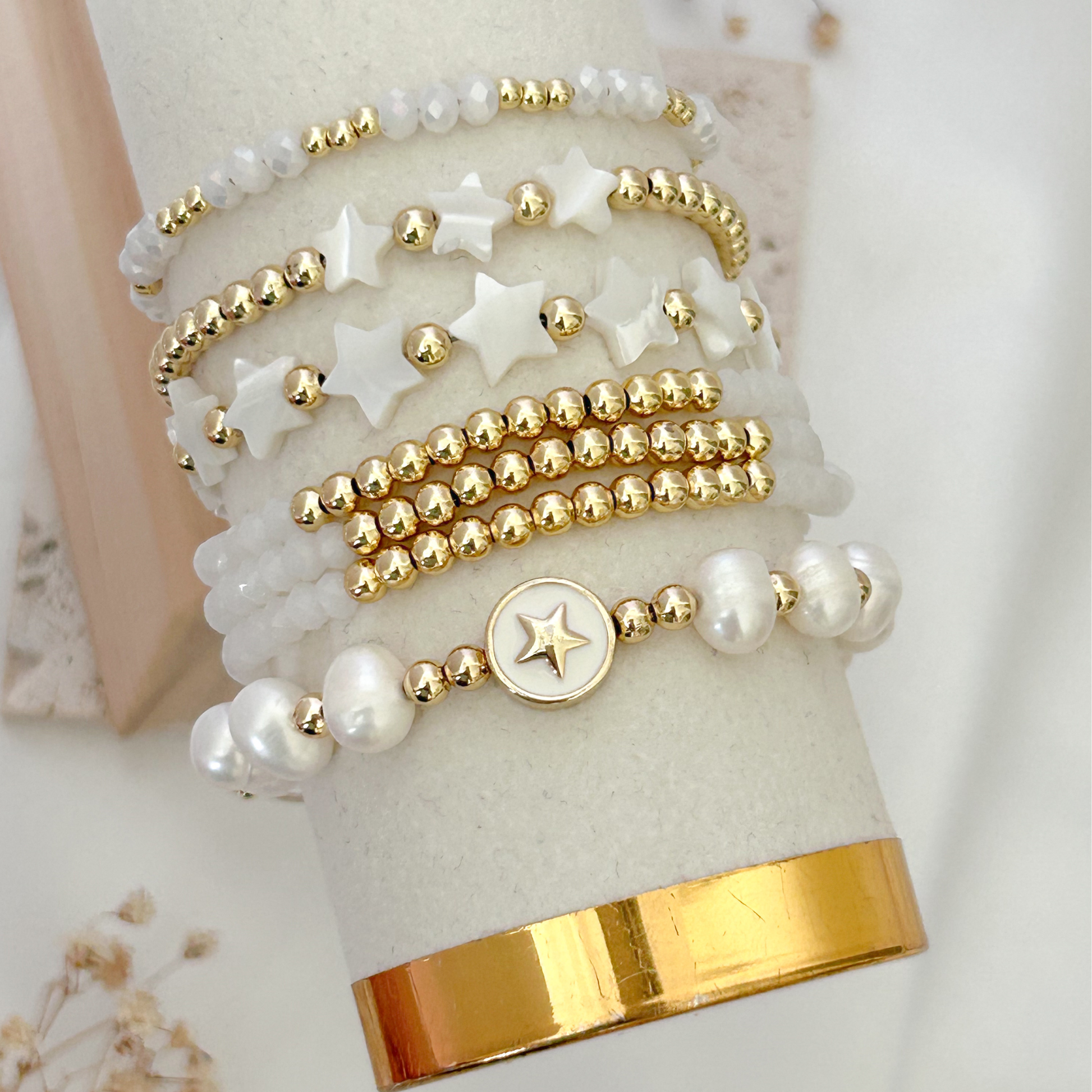 Set of gold and pearl beaded bracelets on a white and gold cylindrical stand.