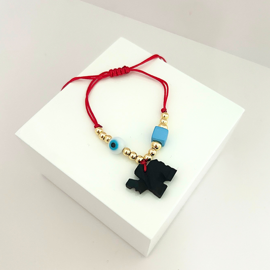 Pulsera roja ajustable con ojo turco, cuentas doradas y dije negro de protección sobre fondo blanco.