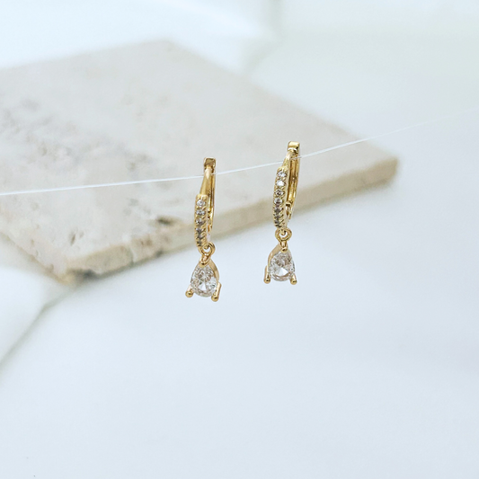 Gold hoop earrings with clear gemstones on a marble surface