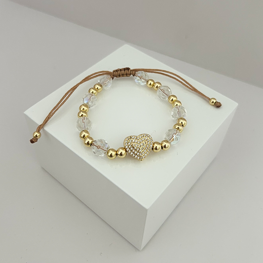 Pulsera ajustable con cristal transparente, cuentas doradas y dije de corazón brillante sobre fondo blanco.
