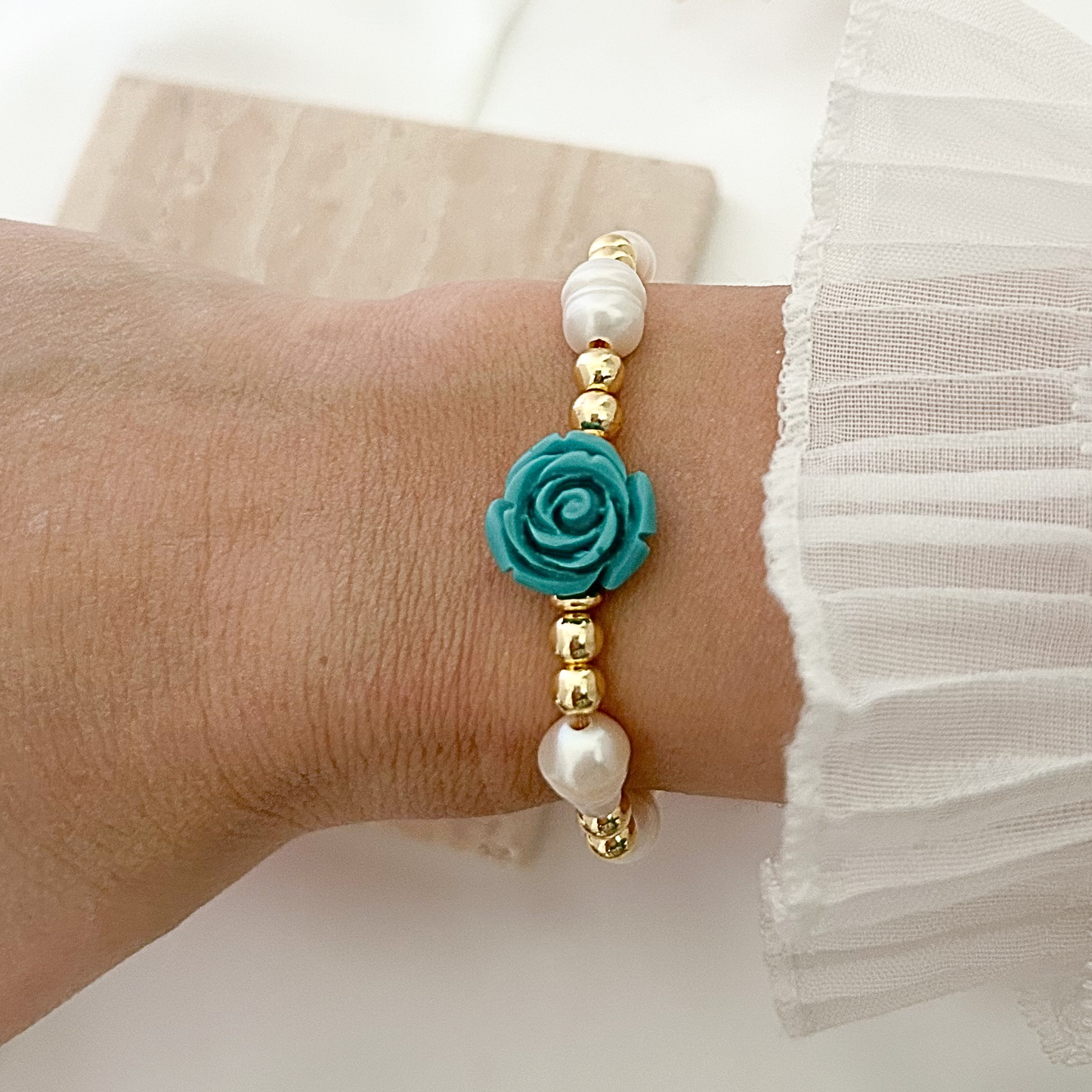 Statement bracelet featuring a turquoise resin rose paired with freshwater pearls and gold-tone beads, worn on the wrist for a sophisticated look.