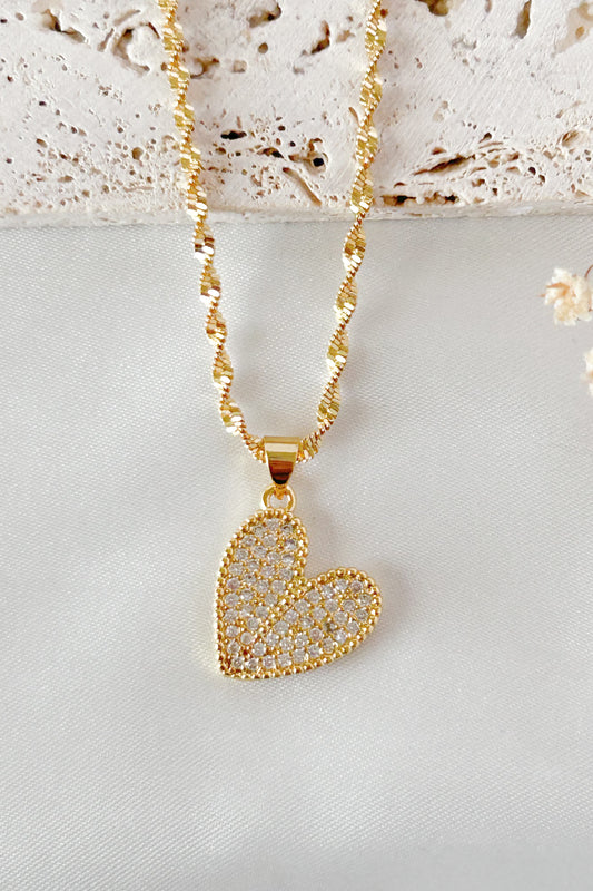 Gold heart-shaped pendant necklace on a light gray surface with a textured beige background