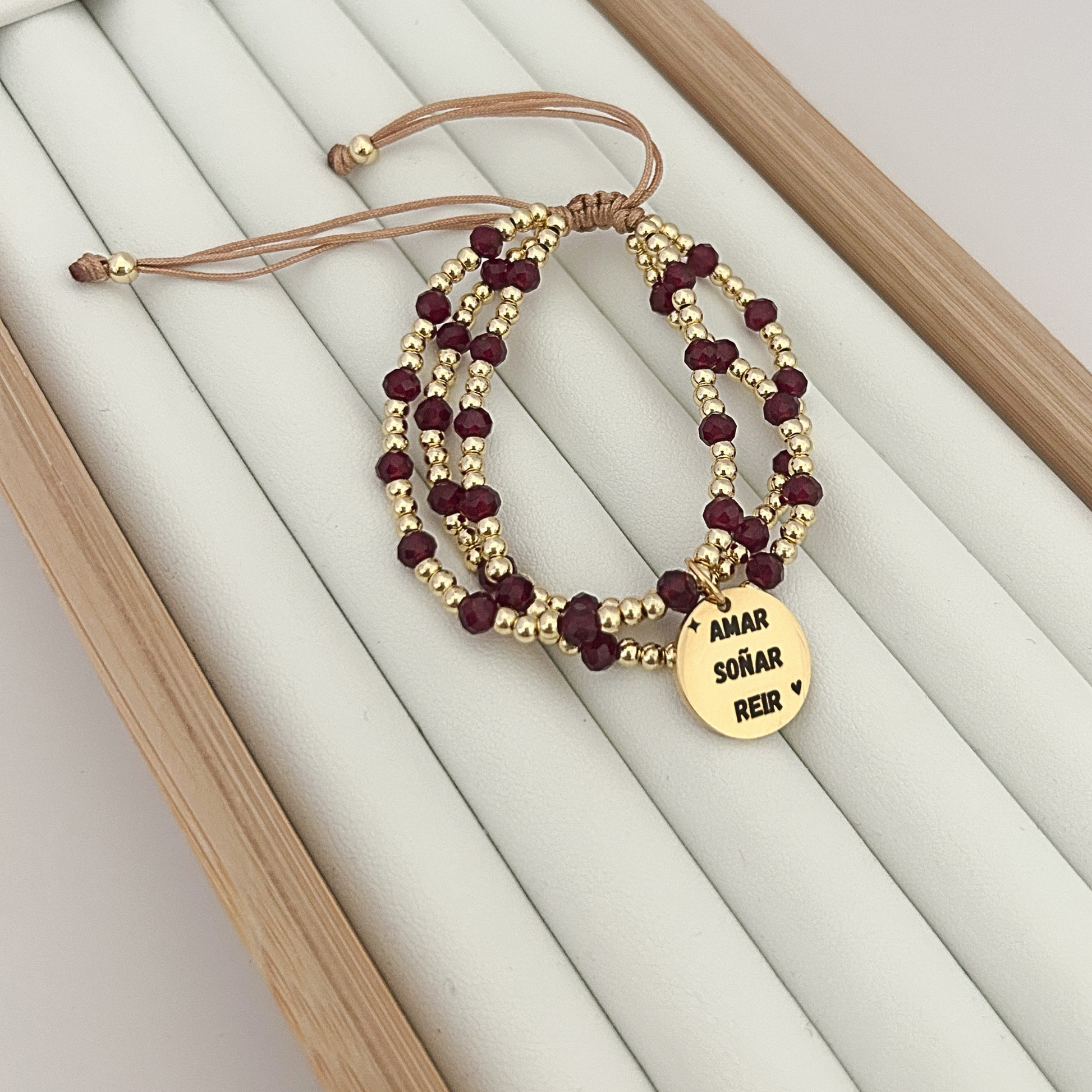 Adjustable burgundy bead bracelet with gold charm and layered wrap design on jewelry tray.