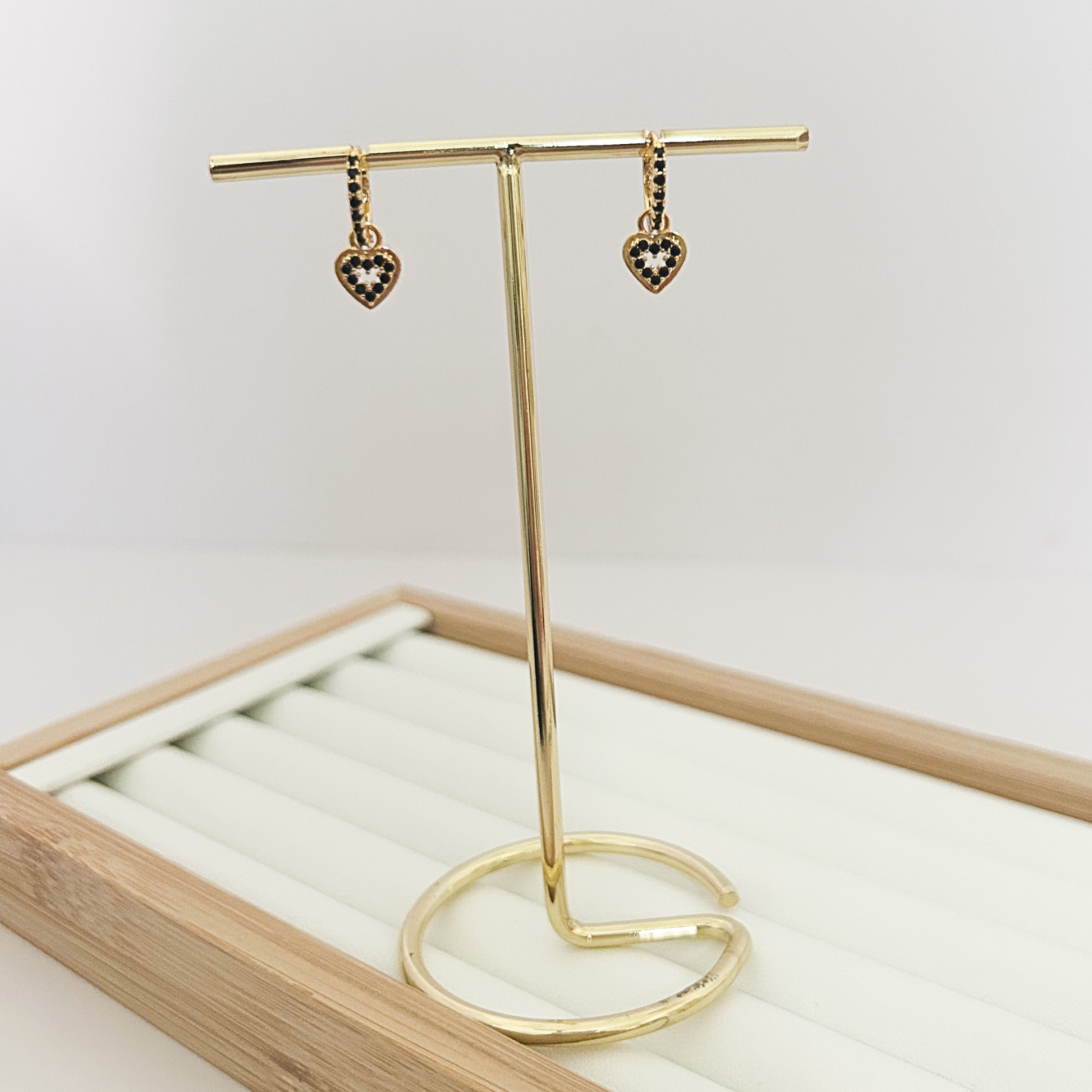 Gold huggie hoop earrings with black pavé heart charm dangle on jewelry stand