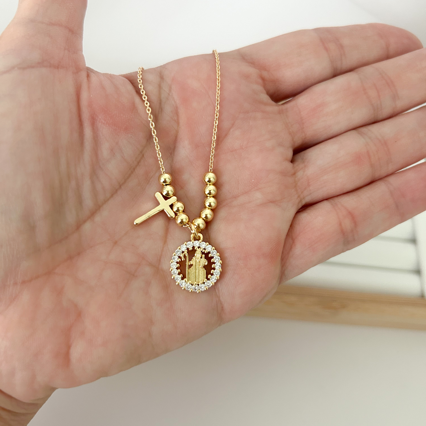 Gold beaded necklace with Divina Pastora medallion and cross charm on linen jewelry bust — Citrika