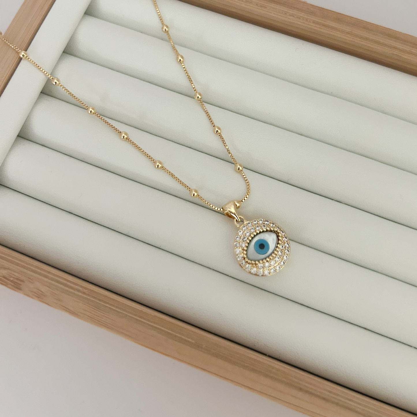 Gold evil eye pendant necklace with blue enamel and zirconia halo on gold chain on white background — Citrika