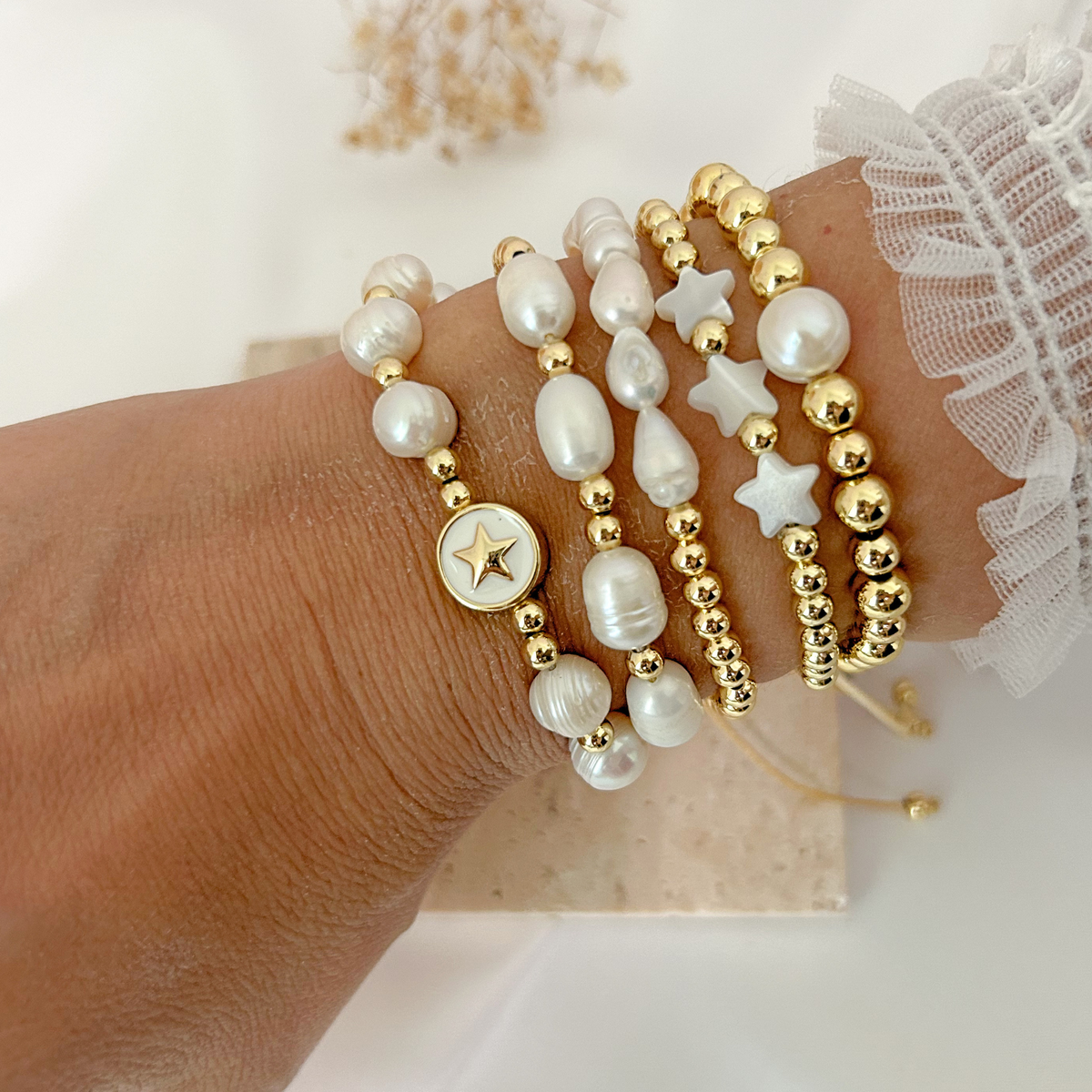 Close-up of layered gold and pearl bracelets with delicate white stars and a star medallion.