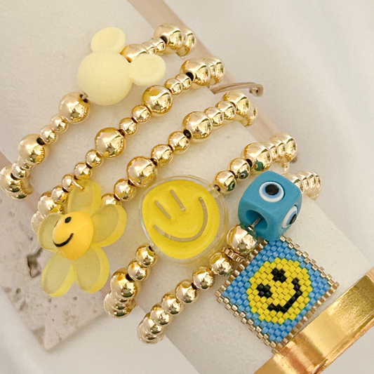 Gold beaded bracelet with smiley face charms on a white background