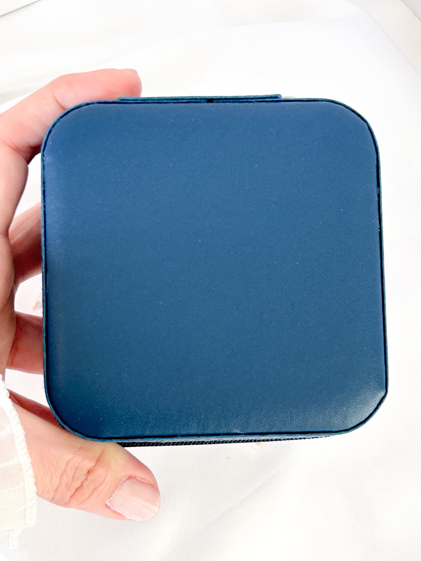 Hand holding a blue square pouch against a white background