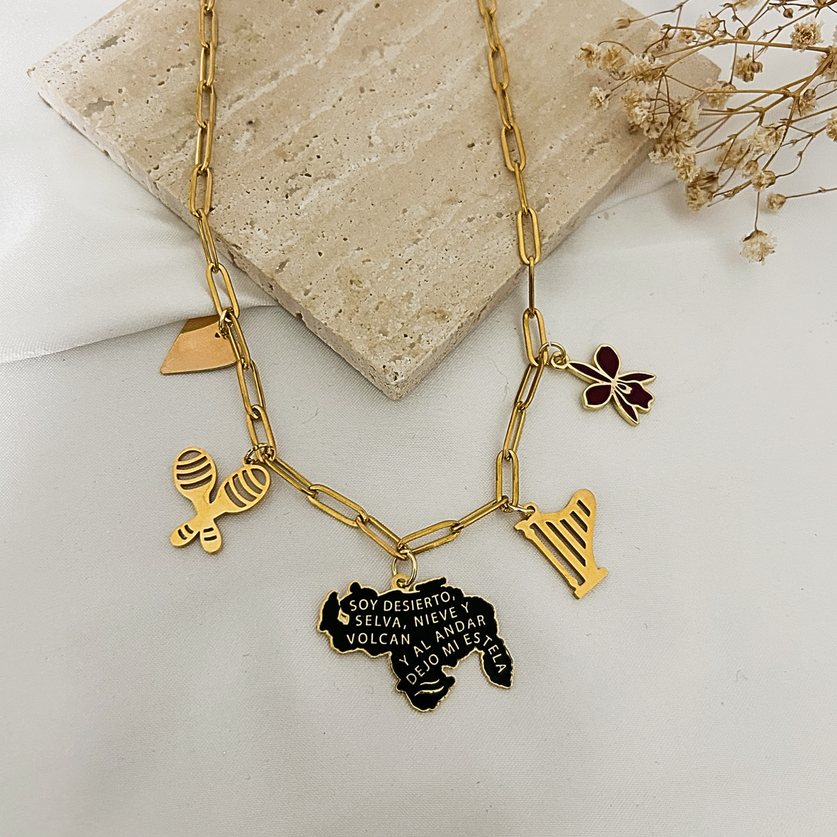 Gold Venezuela charm necklace with map, orchid, harp, and maracas charms on a stone tray