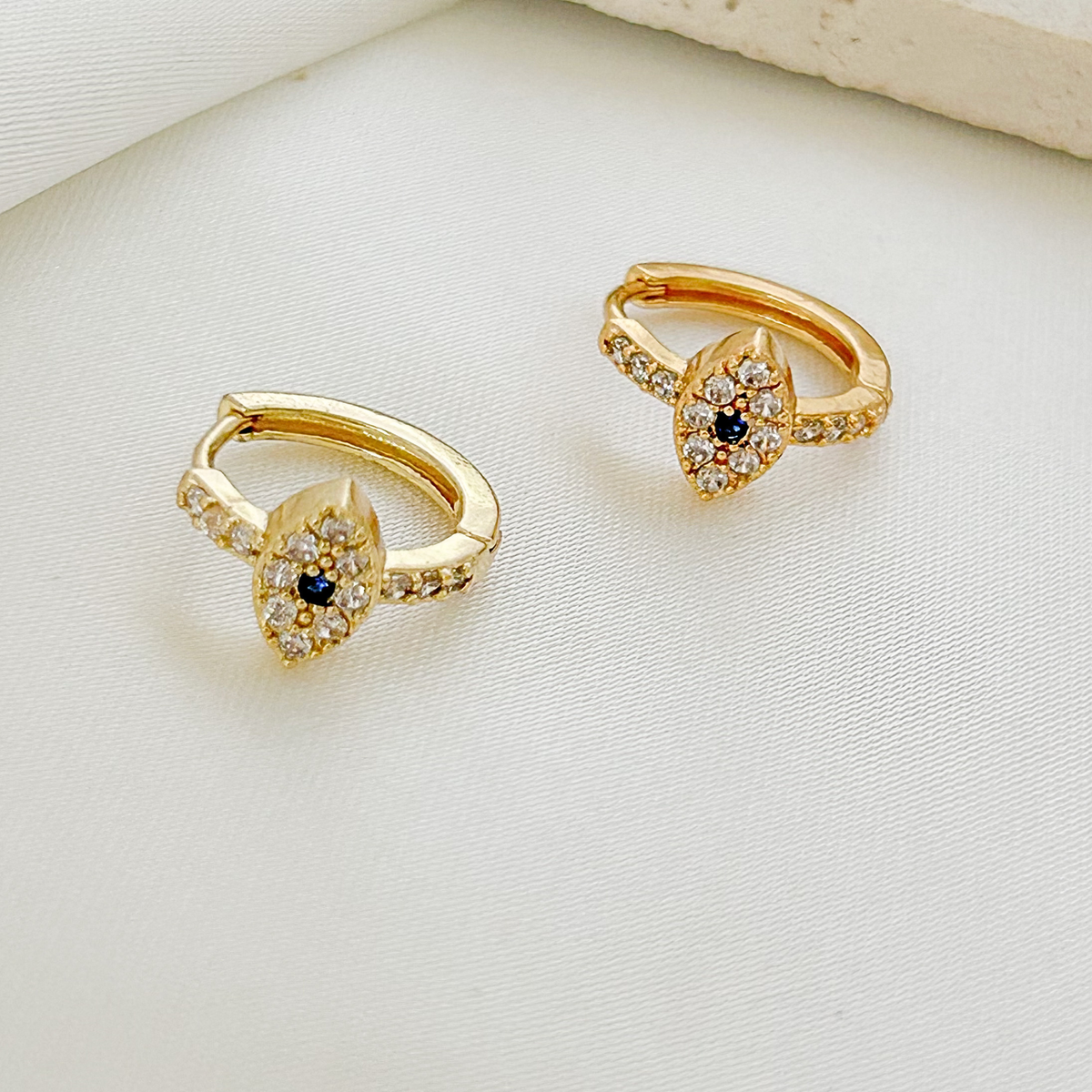 Gold evil eye hoop earrings with sparkling clear crystals and a deep blue center stone.