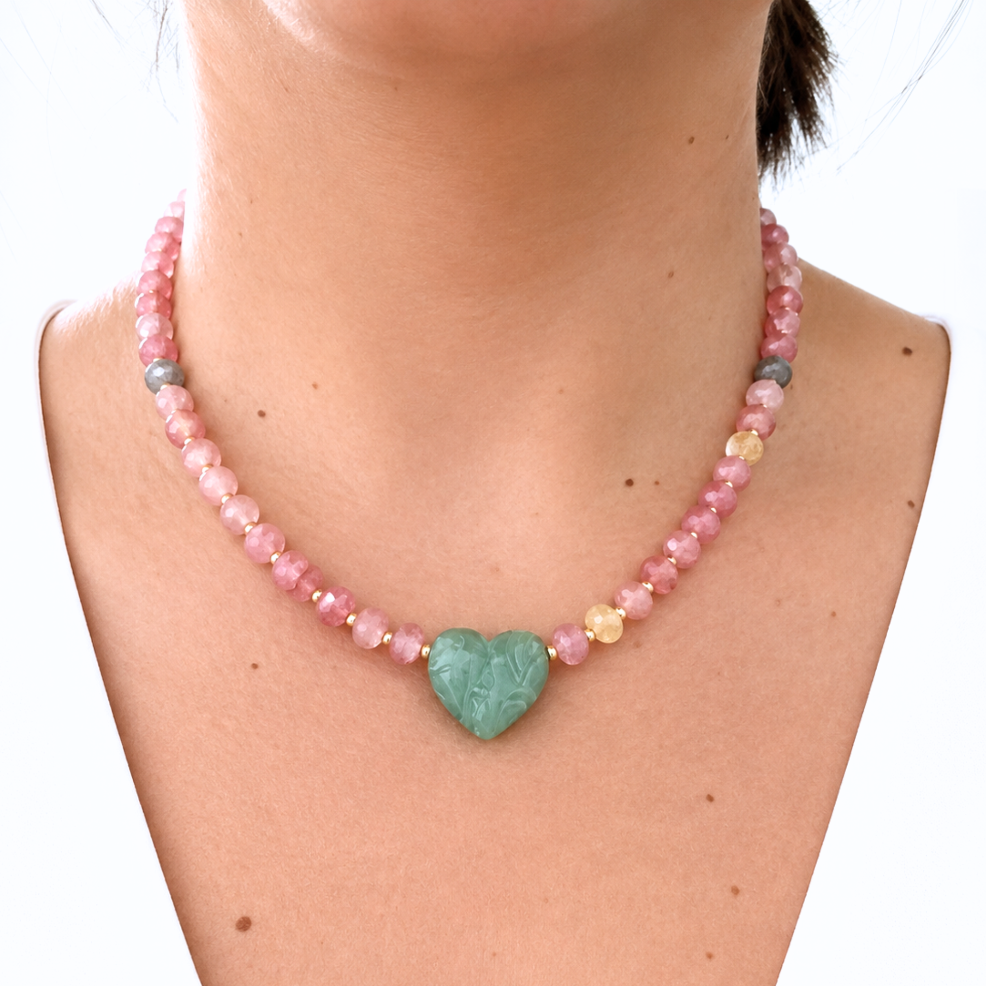 Model wearing a gemstone necklace with soft pink faceted beads, gold accents, and a polished green heart pendant. A feminine and eye-catching piece perfect for everyday wear or special occasions.