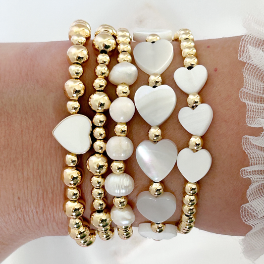 Stack of gold and white heart-shaped beaded bracelets on a wrist.