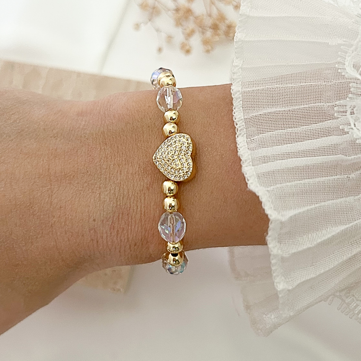 Elegant bracelet featuring faceted crystal beads, gold-tone accents, and a pavé heart charm, styled on the wrist against a soft neutral background.