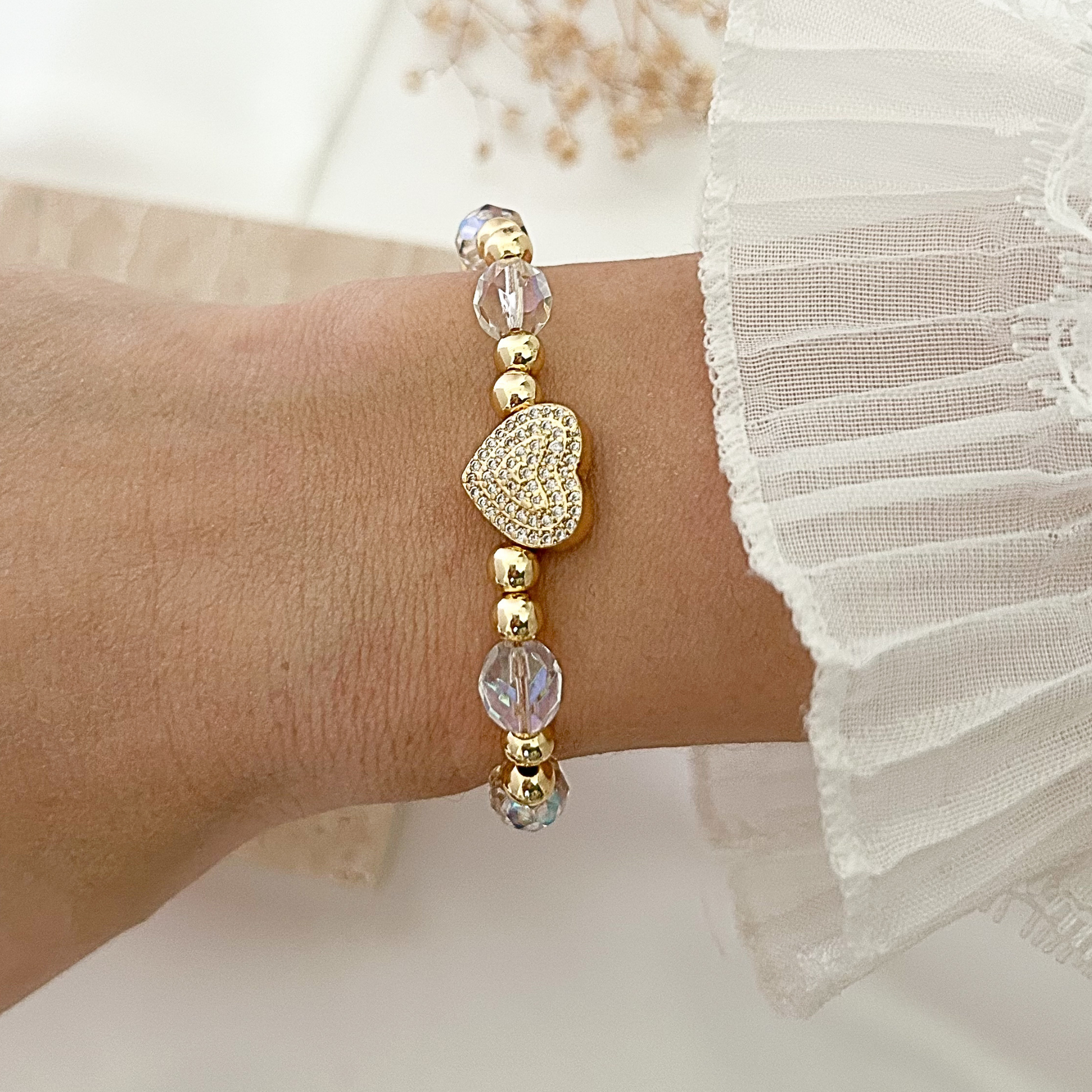 Elegant bracelet featuring faceted crystal beads, gold-tone accents, and a pavé heart charm, styled on the wrist against a soft neutral background.