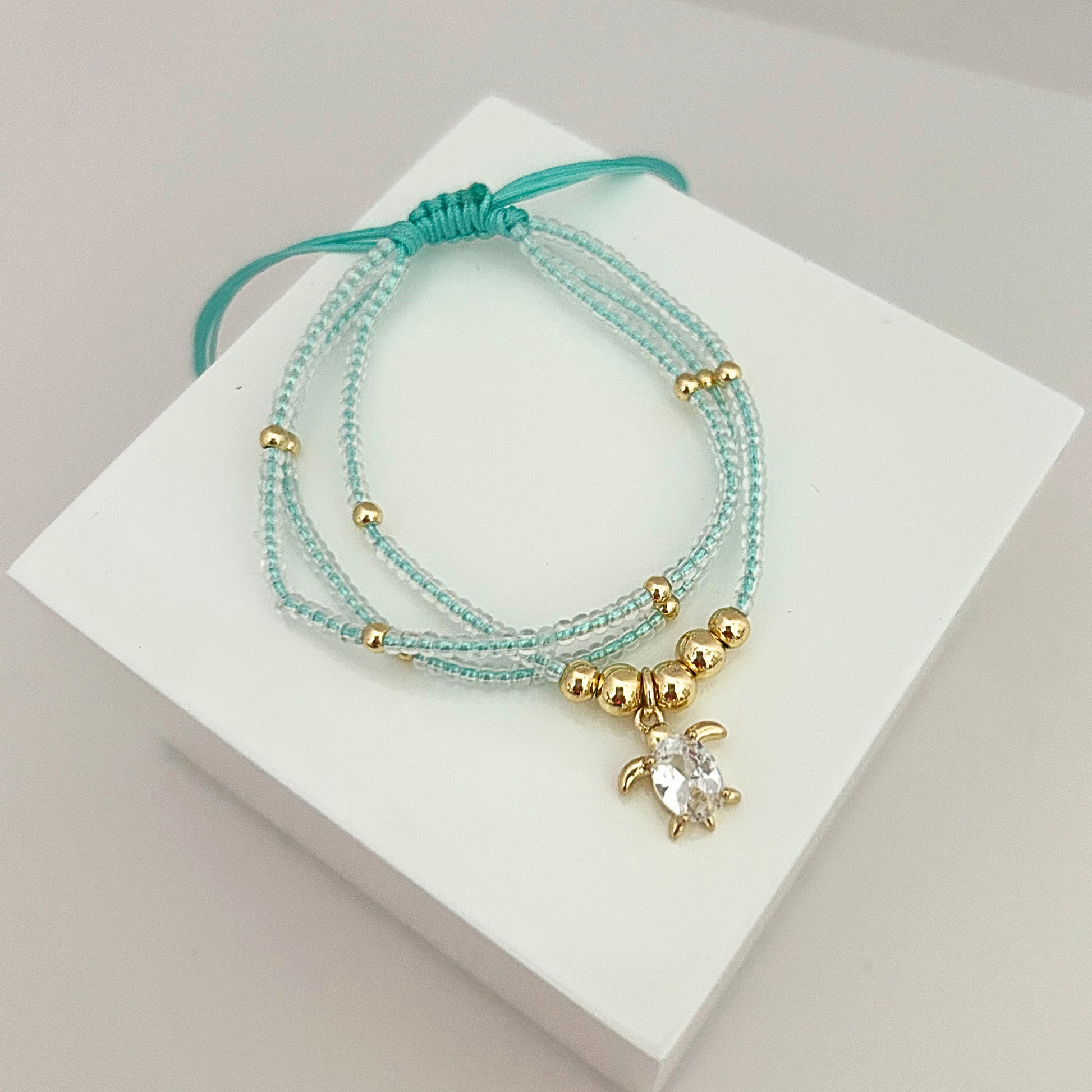 Adjustable sea turtle bracelet featuring delicate light aqua seed beads, gold-tone accents, and a sparkling crystal turtle charm.