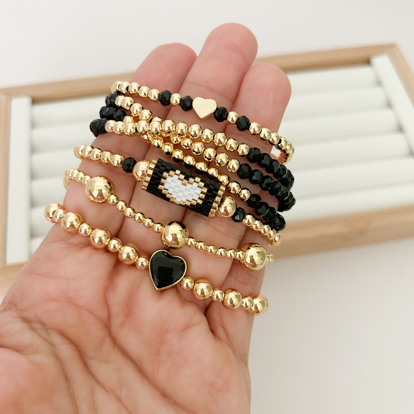 Five black and gold bracelets with miyuki weave and heart charm held in hand