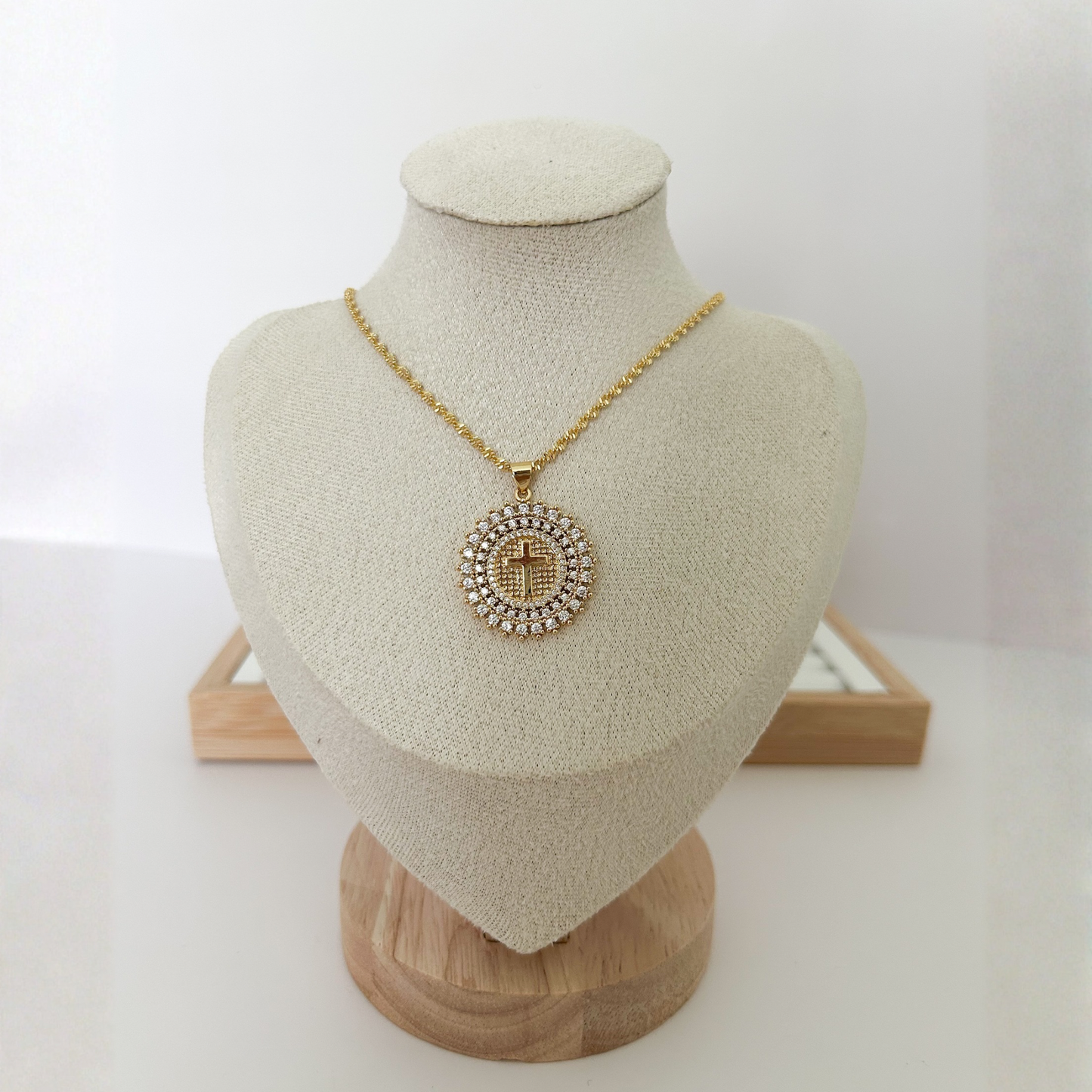 Gold Christian cross medallion necklace for women on beige jewelry display.