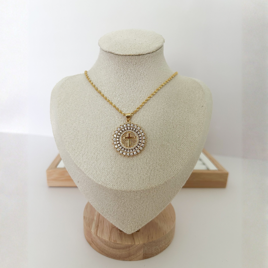 Gold Christian cross medallion necklace for women on beige jewelry display.