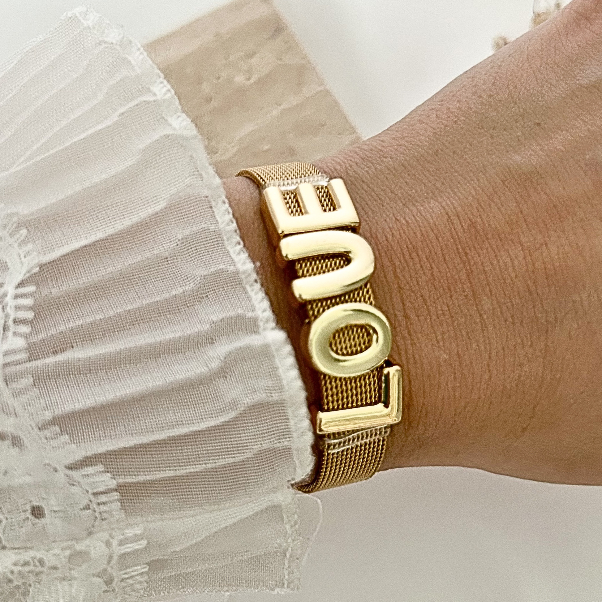 Gold mesh bracelet worn on the wrist, showcasing a polished LOVE design that adds a chic and meaningful statement to any outfit.