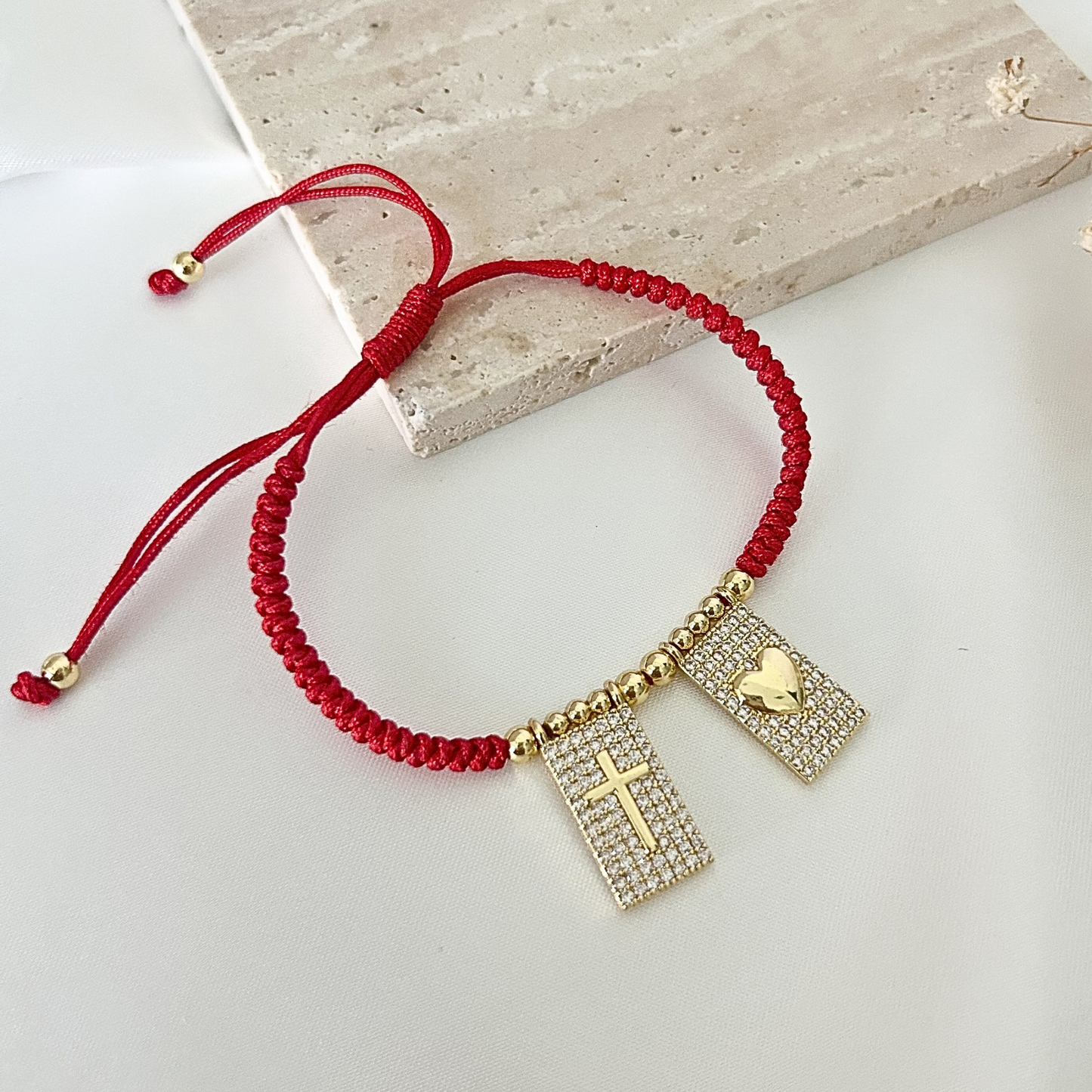 Handcrafted red adjustable bracelet with pavé crystal charms, featuring a gold cross and heart motif against a minimalist background.