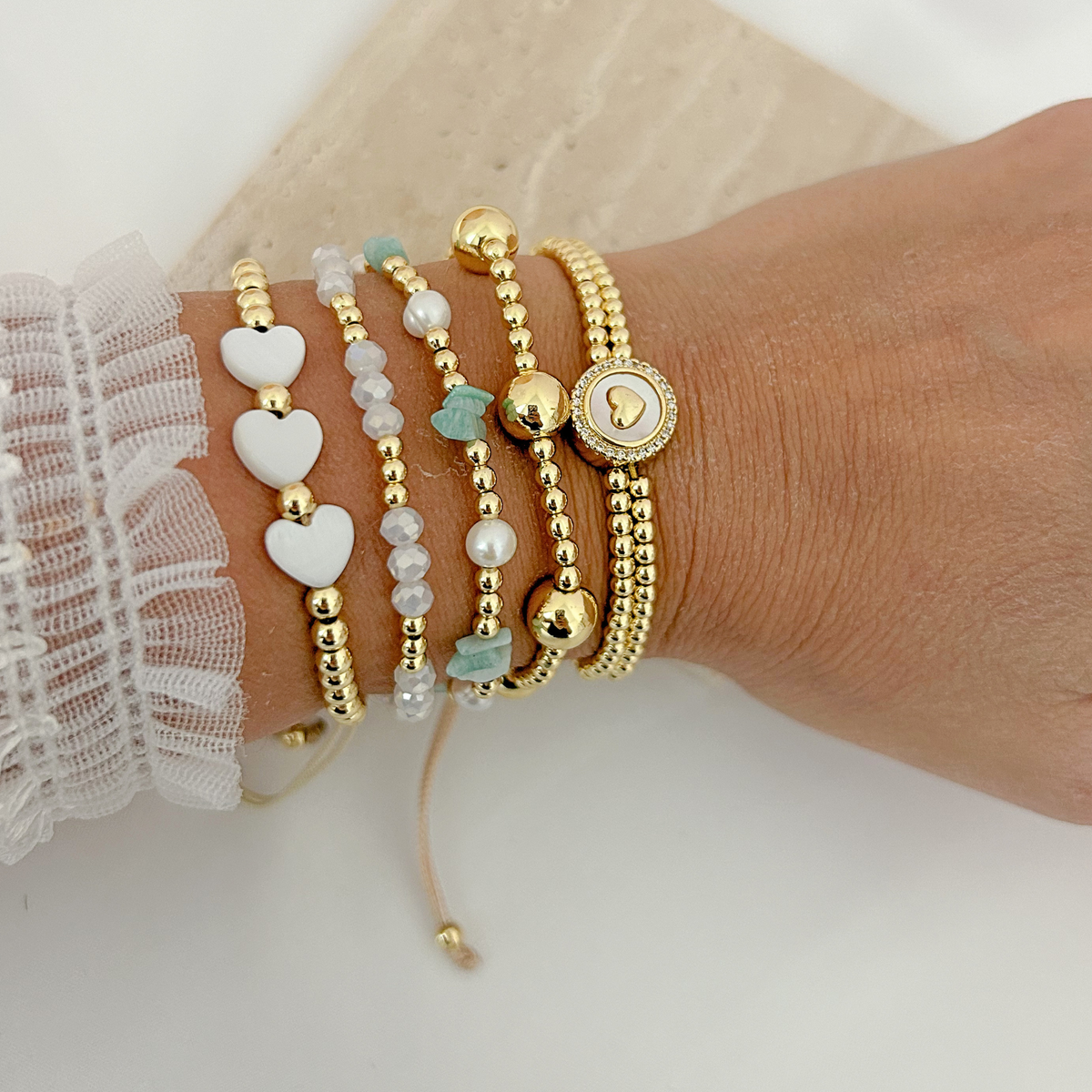 Layered gold beaded bracelets with white heart charms, turquoise stones, pearls, and a round heart centerpiece.