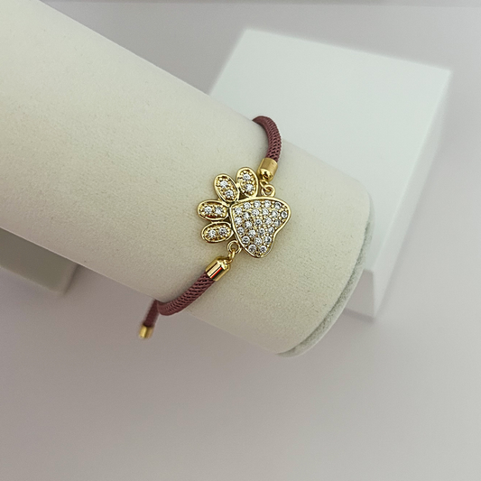 Pulsera ajustable para amantes de las mascotas con huella dorada incrustada de circonias sobre cordón rosa malva.