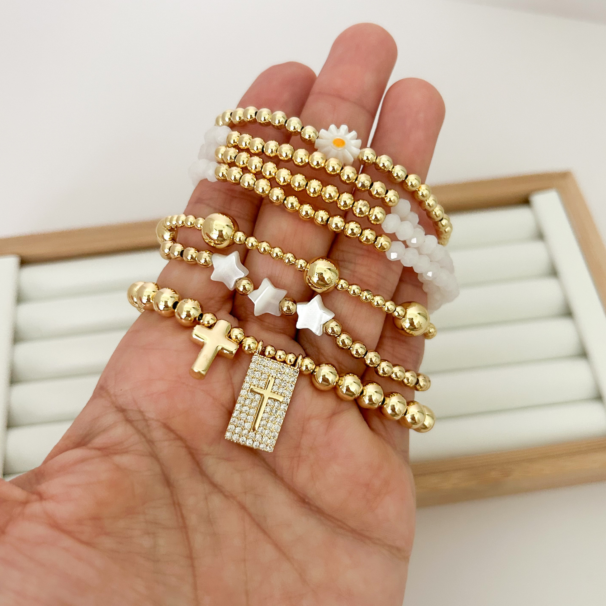 Five gold bracelets with daisy charm, stars and cross pendants held in hand