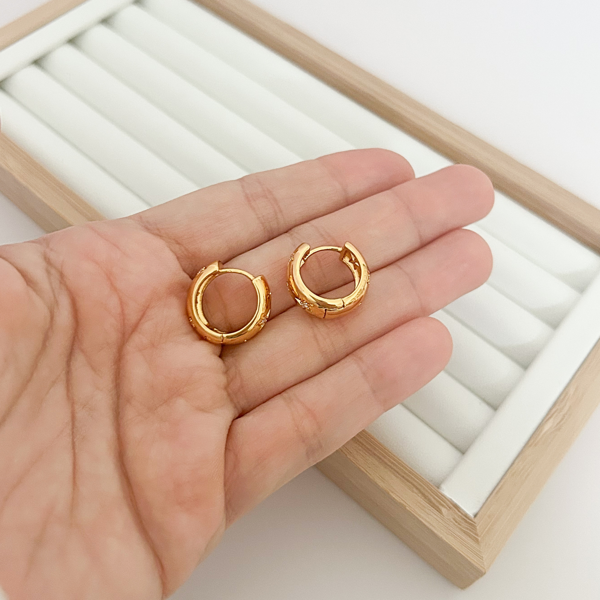 Pair of wide band gold star huggie hoop earrings held in open palm