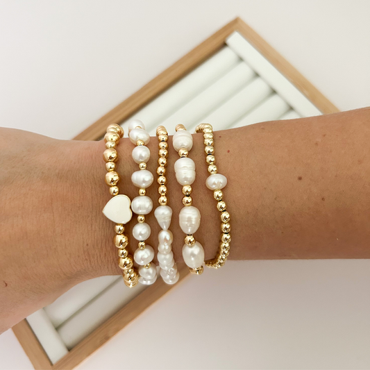 Gold beaded bracelet stack with freshwater pearls and white heart styled on wrist