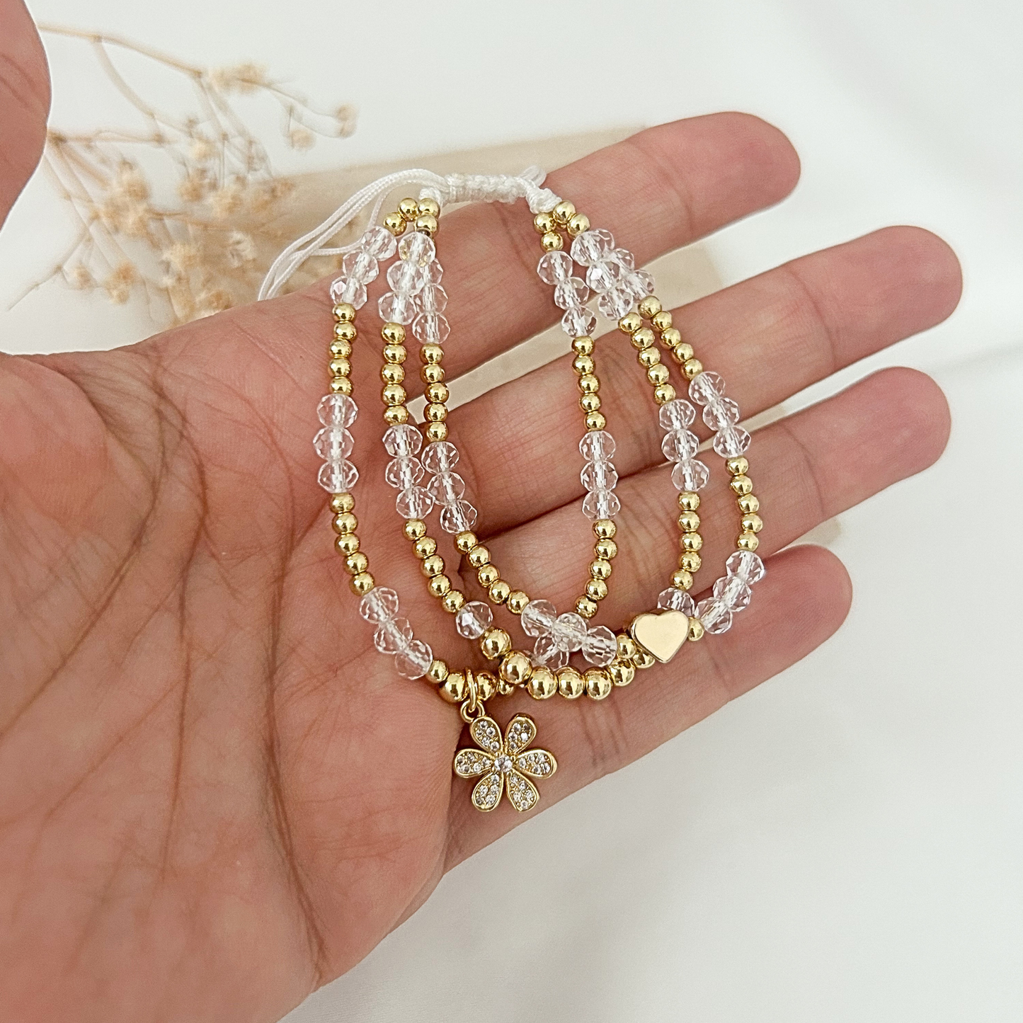 Crystal beaded bracelet with heart charm and cubic zirconia flower charm in hand