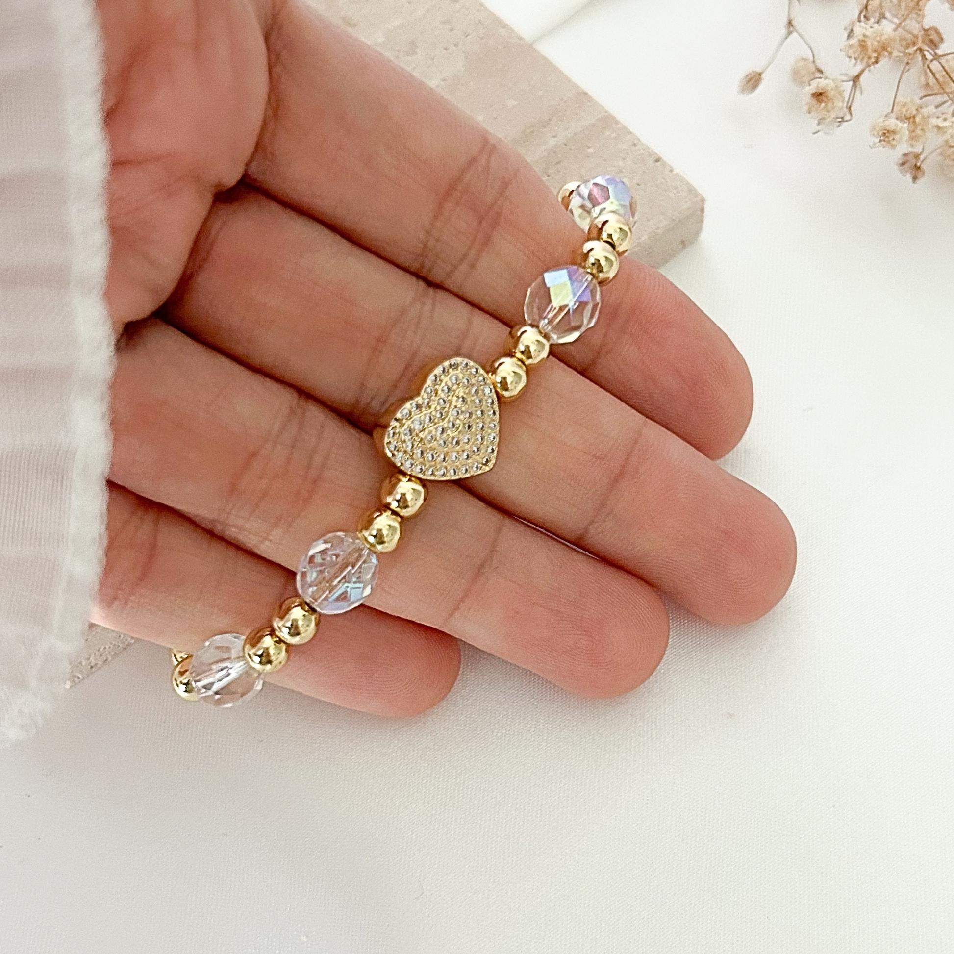 Close-up of a handmade bracelet with shimmering crystal beads, gold-tone beads, and a sparkling heart centerpiece adorned with clear stones.