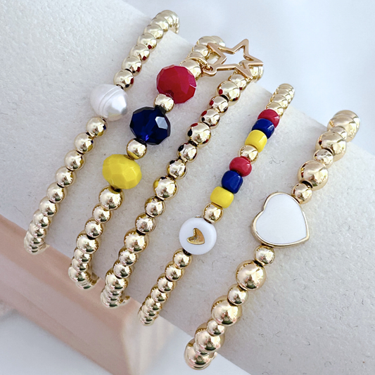 Gold beaded bracelets with colorful beads and heart charm on a white background